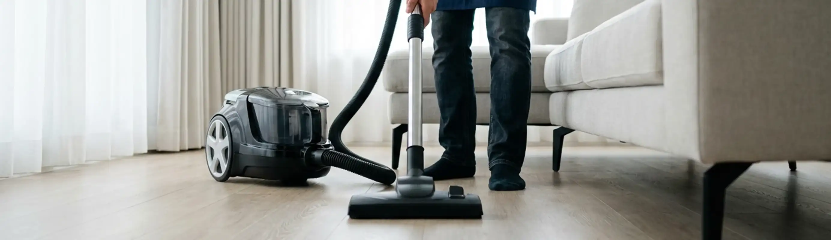 Professional house cleaner vacuuming a living room floor with a canister vacuum cleaner, El Paso, TX.