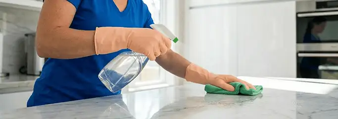 Maid service worker spraying and wiping a kitchen countertop with a microfiber cloth for sanitizing, El Paso, TX.