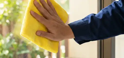 House cleaner wiping a glass window with a yellow microfiber cloth for streak-free cleaning, El Paso, TX.